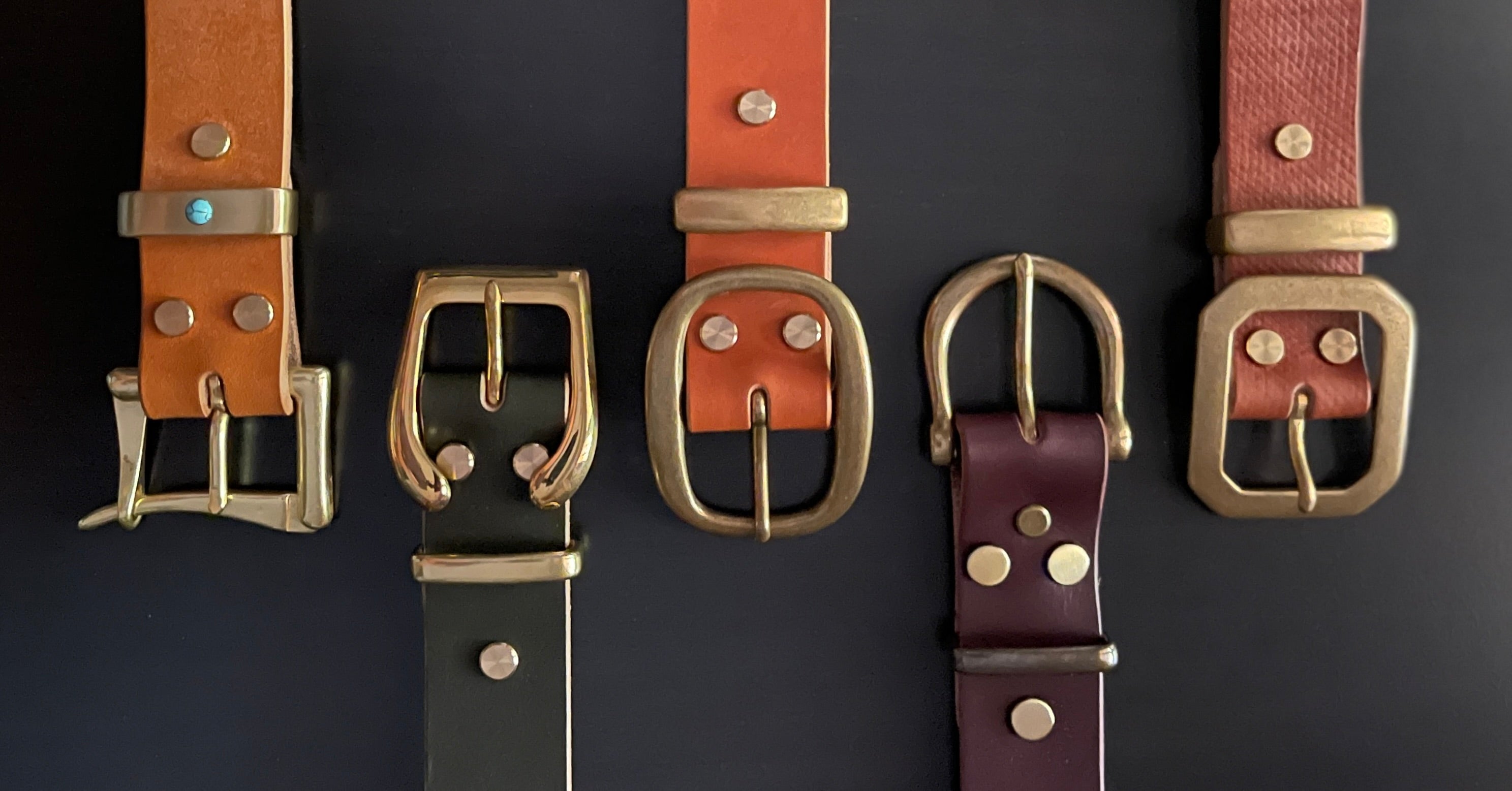 Five leather belts of various colors with brass buckles arranged in a row