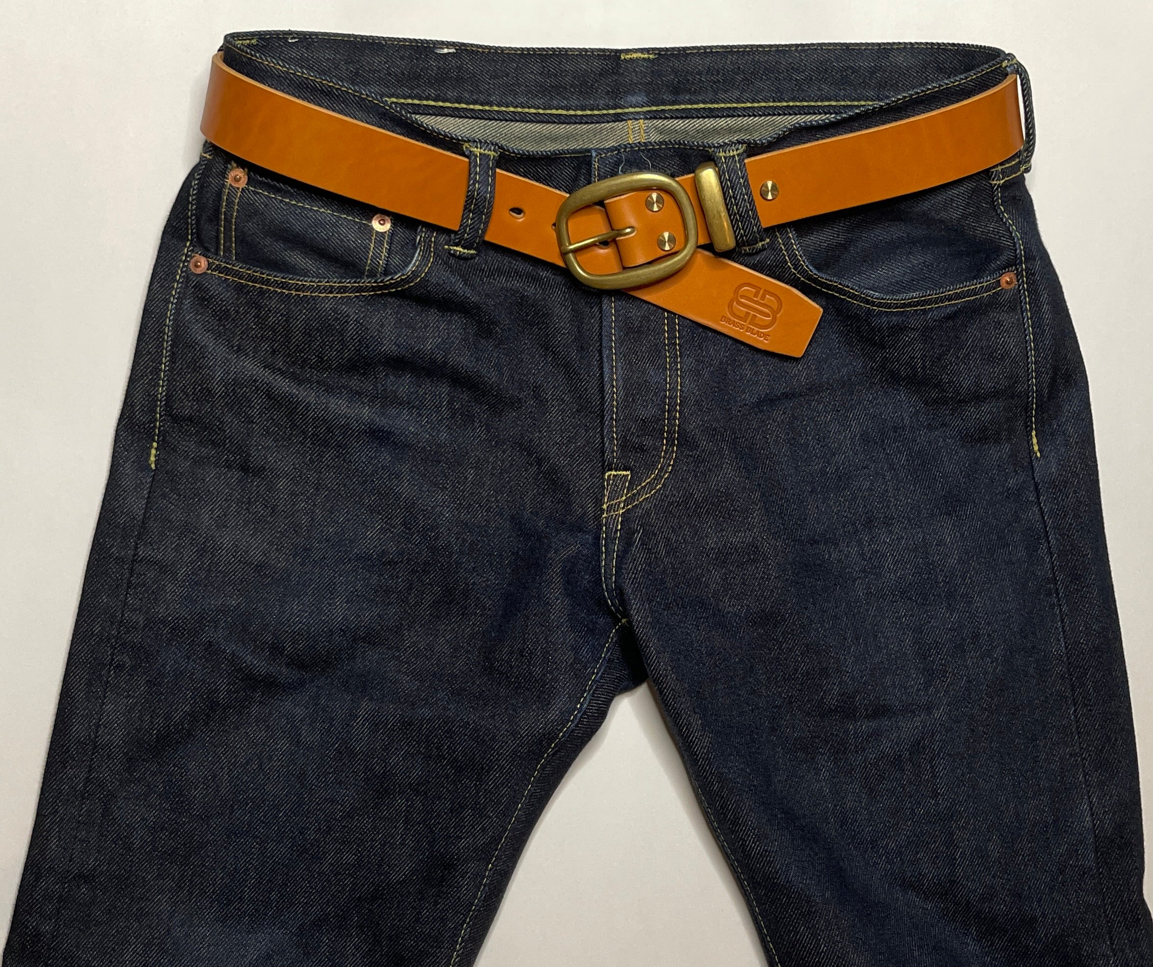Dark blue jeans with a brown belt and brass buckle on a white background