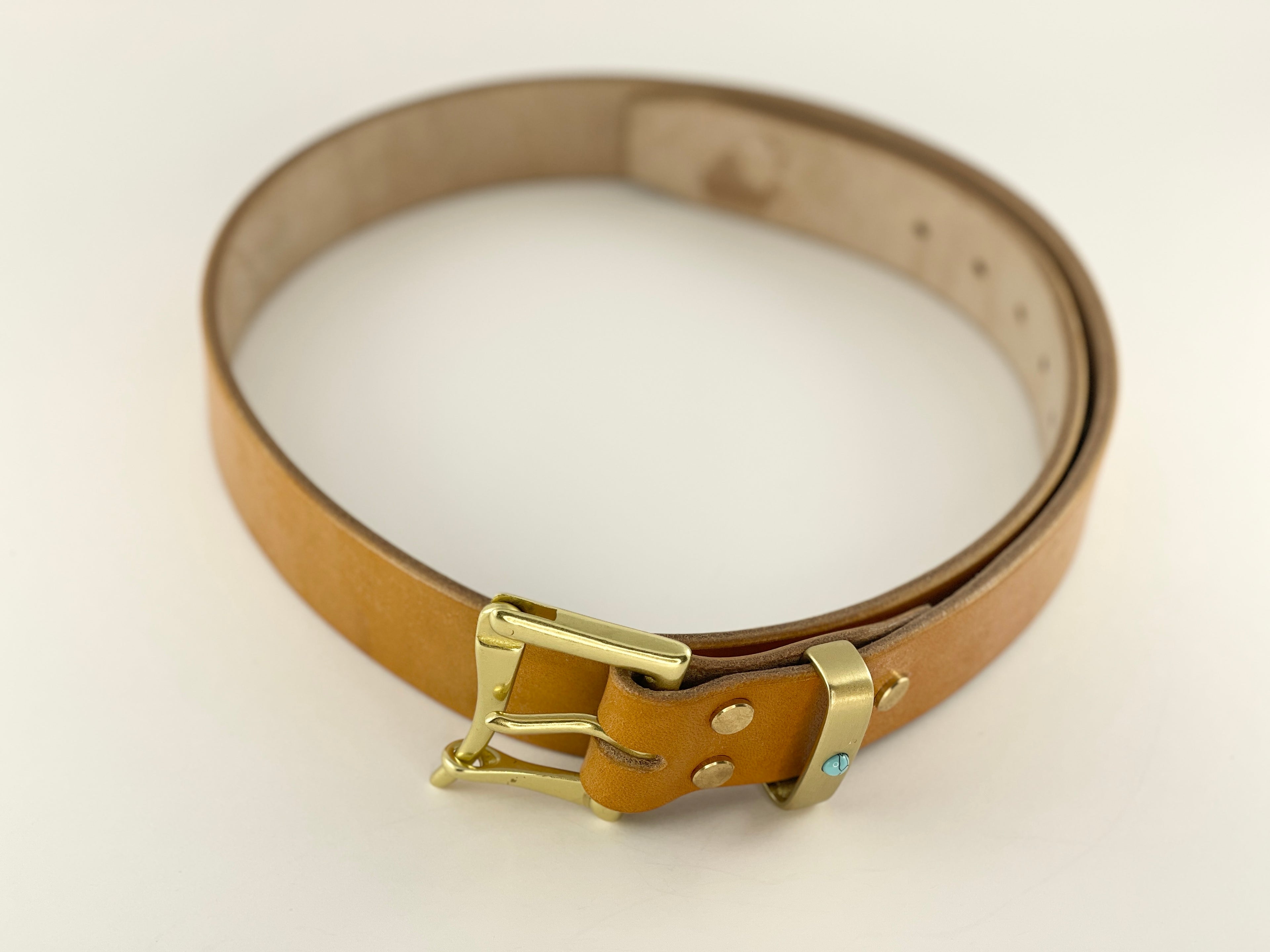 Tan leather belt with a gold buckle on a light beige background