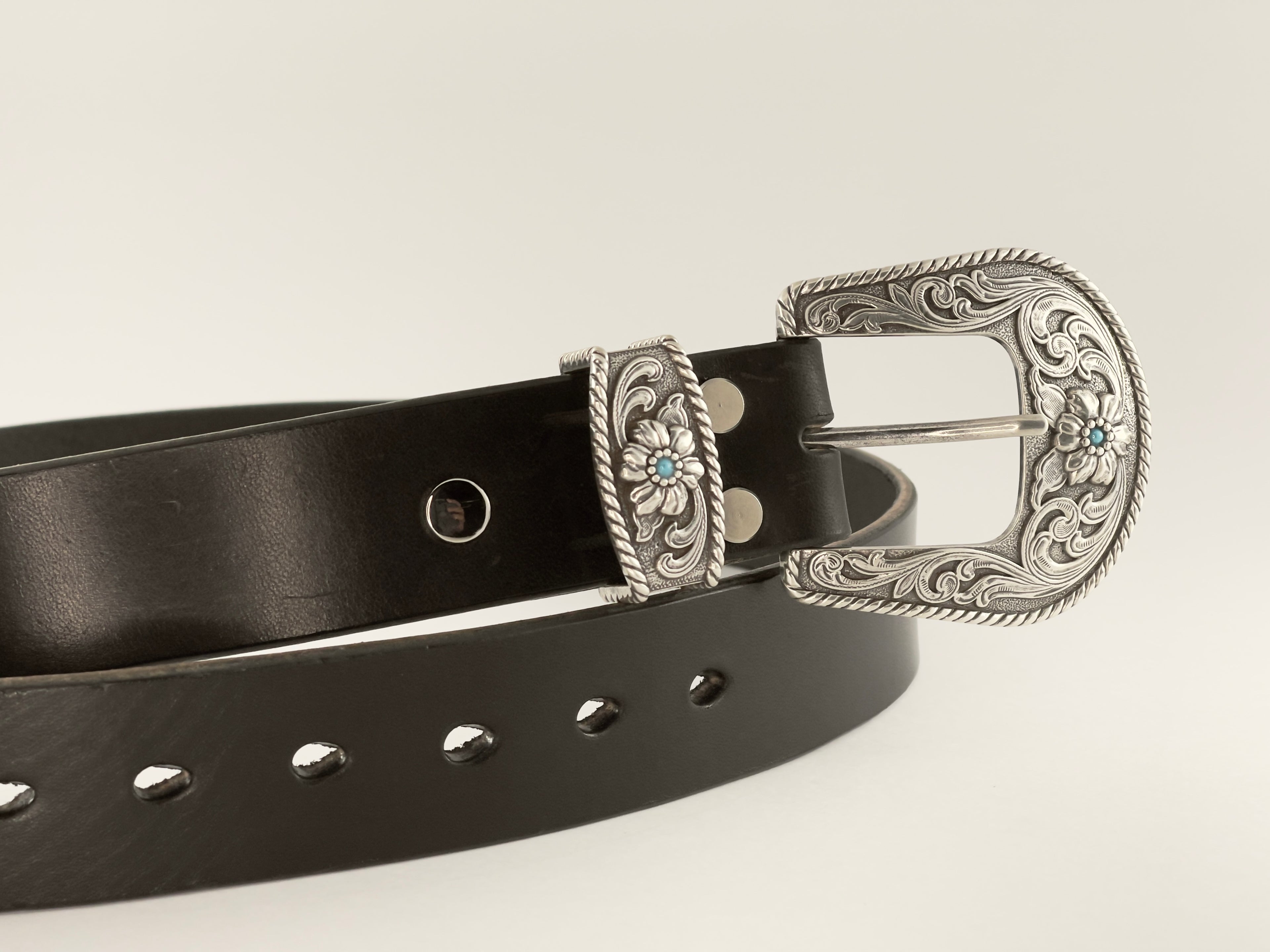 Black belt with a silver floral buckle on a light gray background