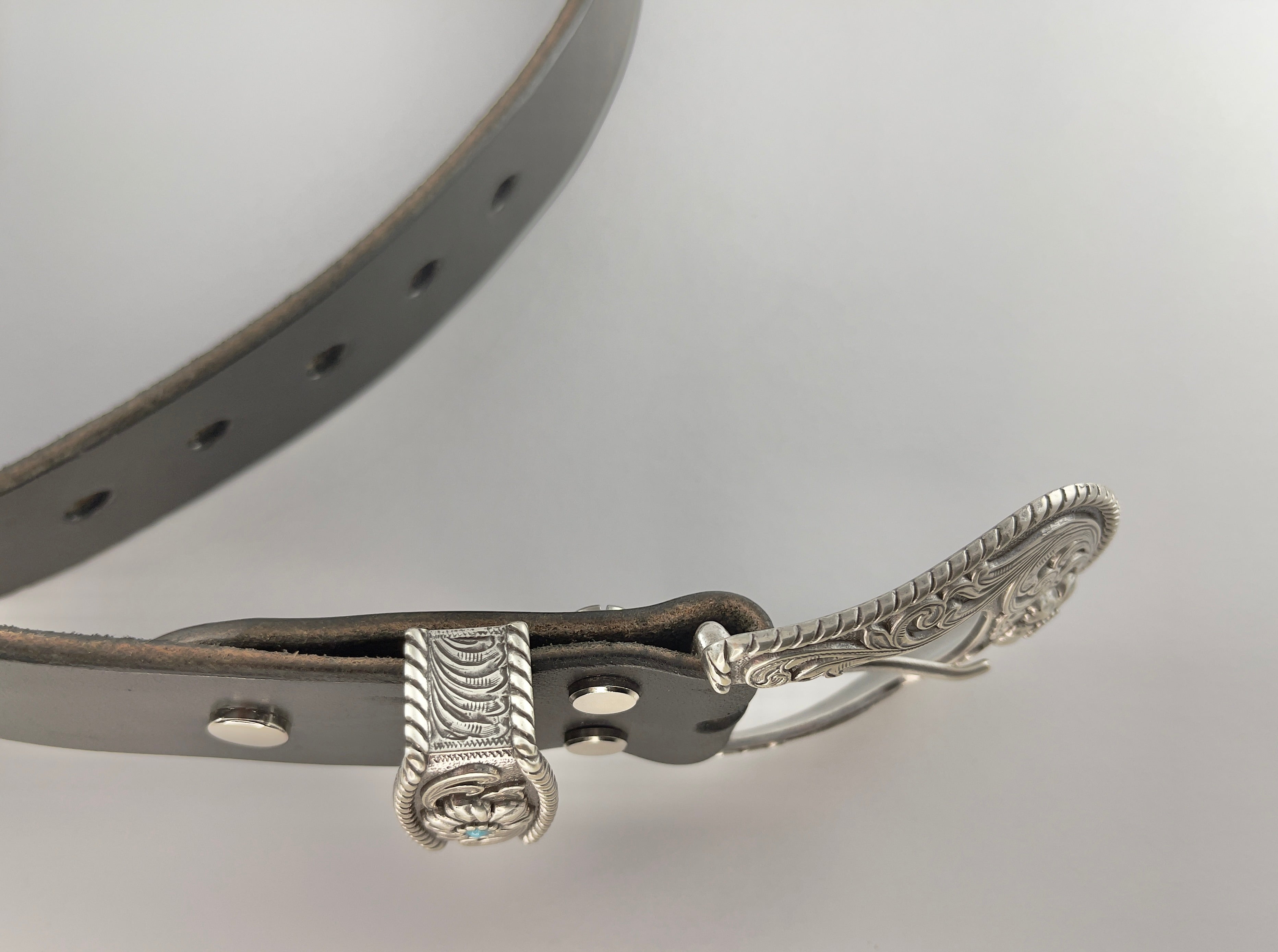 Black leather belt with silver buckle on a light gray background