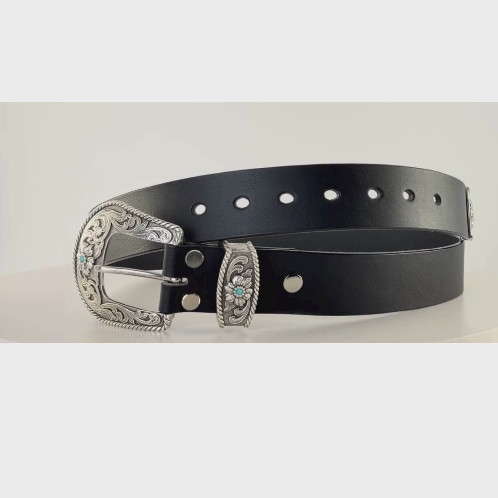 Video of a black western cowboy leather belt with silver buckle and keeper adorned with turquoise stones, rotating on a mechanical carousel