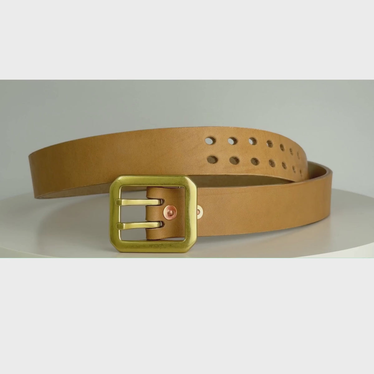 A thick natural leather belt with a large rectangular dual-pronged  brass buckle, on a white carousel.  The carousel spins around, showing the belt in 360 degrees.