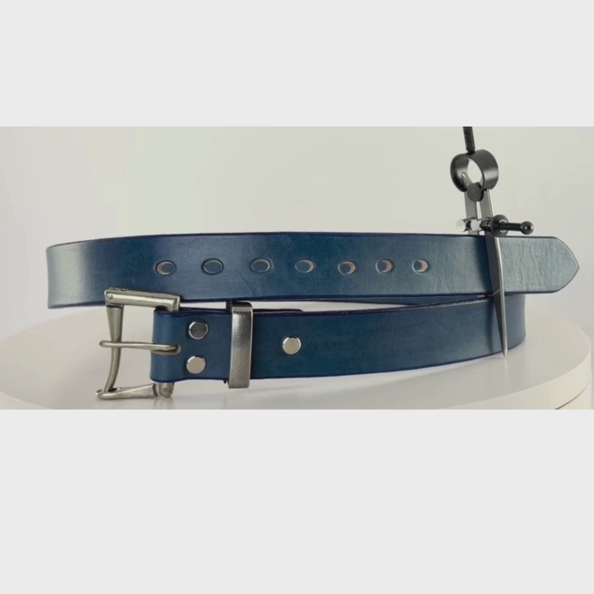 Video of a blue leather belt with a silver buckle rotating on a white carousel.