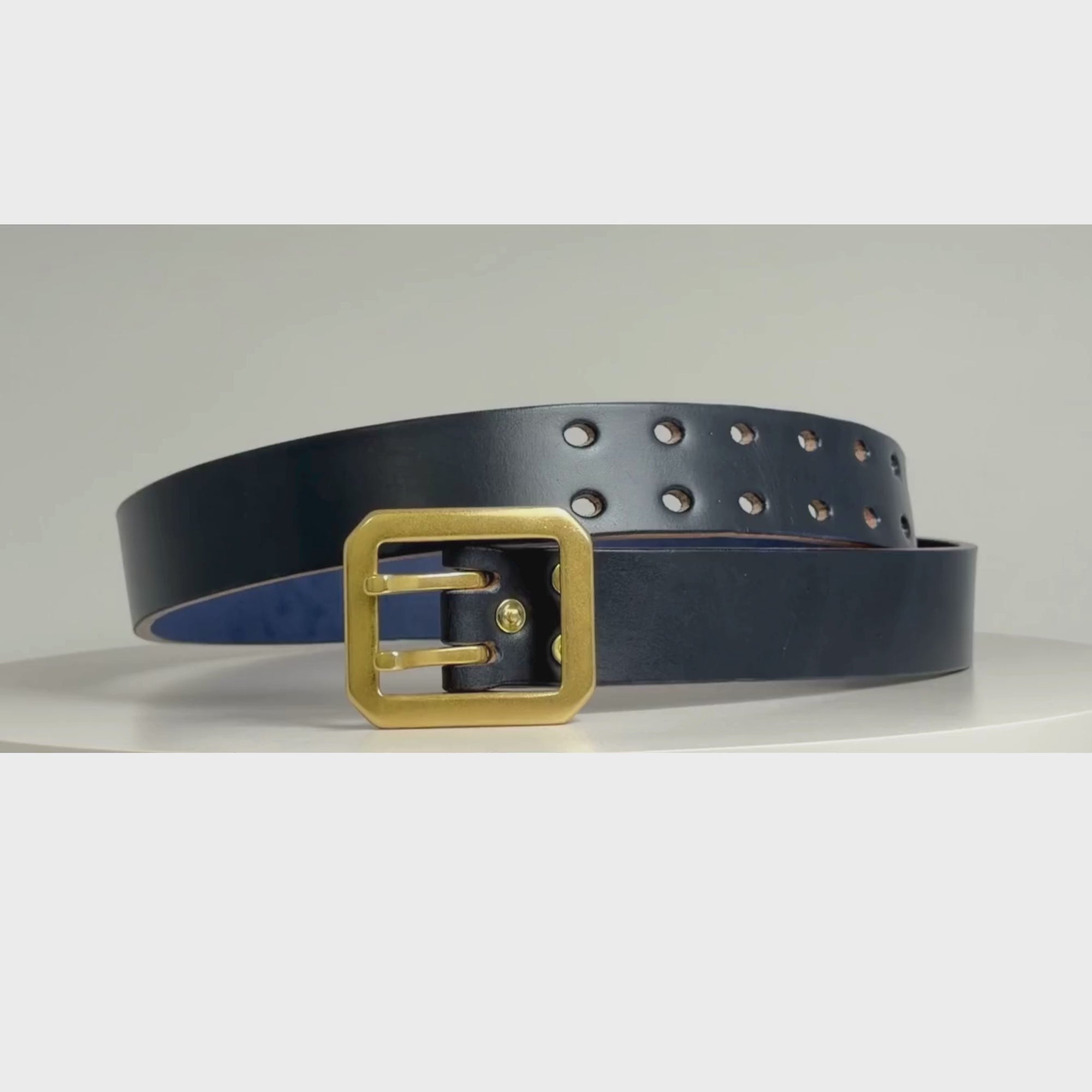 Video of a navy leather belt with brass buckle and rivets on a white carousel.